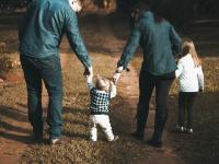 Eltern mit zwei kleinen Kindern laufen auf einem Waldweg
