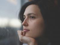 Frau schaut nachdenklich aus dem Fenster (Portrait)